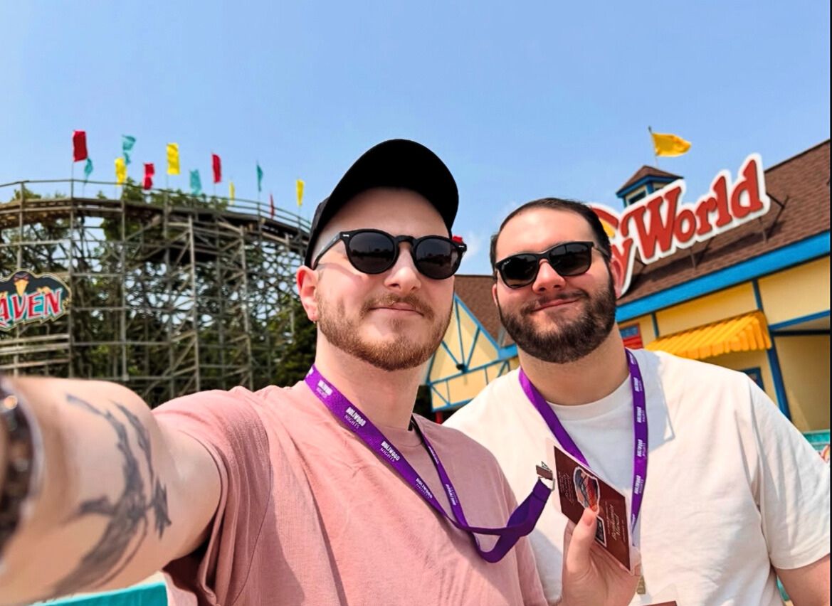 Two people pose by the Holiday World sign and The Raven roller coaster