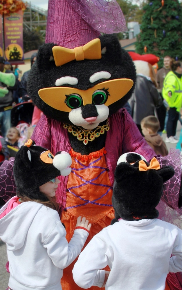 Kitty Claws giving hugs to two young girls with Kitty Claws hats on during Happy Halloween Weekends at Holiday World.